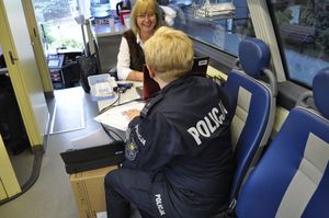 Na zdjęciu widoczne dwie kobiety z czego jedna siedząca tyłem w policyjnym mundurze.