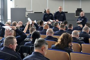 Zdjęcie przedstawia członków komisji, którzy rozdają policjantom arkusze testowe