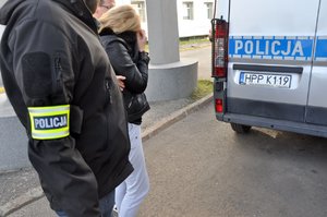 Na zdjęciu dwaj nieumundurowani policjanci prowadzą do pomieszczenia dla osób zatrzymanych jedną z kobiet