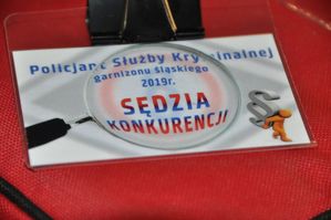Zdjęcie kolorowe. Na zdjęciu znajduje się plakietka z napisem Policjant Służby Kryminalnej garnizonu śląskiego 2019 Sędzia Konkurencji
