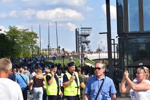 Na zdjęciu widać dwóch policjantów w tłumie ludzi zebranych na placu przed Spodkiem, policjanci rozmawiają przez krótkofalówki, w tel widać szyb przy Muzeum Śląskim