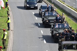 Na zdjęciu widać kolumnę pojazdów z Prezydentem Polski która jedzie ulicą obok stoją policjanci i żandarmi zabezpieczający defiladę