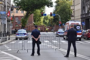 Na zdjęciu widać policjanta przed barierkami obok stoi karetka w oddali widać policjantów ruchu drogowego