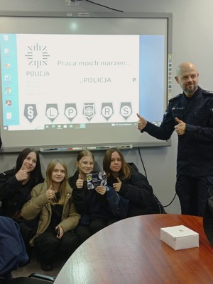 Zdjęcie. Grupa uczniów i umundurowany policjant w sali podczas pamiątkowego zdjęcia