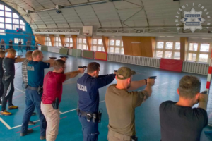 Na zdjęciu policjanci w szeregu trenują z bronią na sali gimnastycznej.