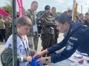 Na zdjęciu mundurowa w trakcie wręczania chłopcu gadzetów promujących zawód policjanta  Ogólnopolskiego Turnieju Klas o Profilu Mundurowym