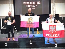 Na zdjęciu 3 zawodnicy na podium. Na 1 i 3 miejscu zawodnicy trzymają biało-czerwoną flagę.