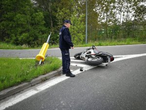 Miejsce zdarzenia drogowego, policjant stoi przy wywróconym na jezdni motocyklu