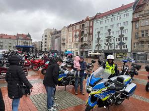 Na zdjęciu policjant stojący obok motocykla służbowego, za mim motocykle i uczestnicy wydarzenia.