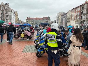 Na zdjęciu policjant, obok niego kobieta, za nimi motocykle i osoby zgromadzone na rynku.