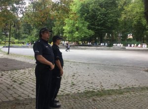 dwóch umundurowanych policjantów stojacych bokiem w parku jasnogórskim, w tle na ławkach siedzący wierni