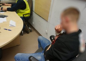 zatrzymany mężczyzna podczas przesłuchiwania przez policjanta wydziału kryminalnego siedząc tyłem do fotografującego