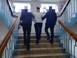 Dwóch nieumundurowanych policjantów prowadzi po schodach zatrzymanego.