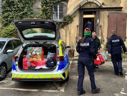 Policjanci ładują paczki do oznakowanego radiowozu.