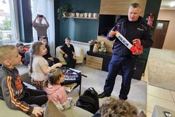 Zdjęcie przedstawia policjanta prezentującego sprzęt policyjny dzieciom.