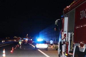Na zdjęciu miejsce wypadku na autostradzie A1 , widoczny policyjny radiowóz na sygnale, policjant w trakcie czynności i wóz strażacki.