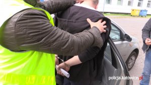 Policjant wprowadza do samochodu podejrzanego o napad mężczyznę