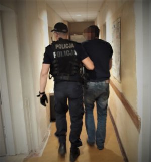 na zdjęciu: zatrzymany mężczyzna doprowadzany przez policjanta na przesłuchanie