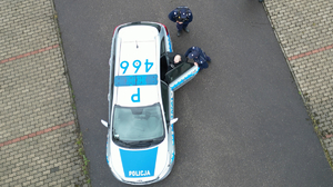 zdjęcie przedstawia policjantów doprowadzających zatrzymanego do radiowozu
