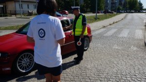 Policjant z wolontariuszką wręczają symboliczne serduszko kierowcy