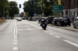 Fotografia kolorowa. Na zdjęciu widoczny policjant jadący na służbowym motocyklu.