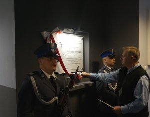 Na zdjęciu policjanci z warty honorowej oraz Pan Jerzy dokonujący zdjęcia szarfy z tablicy upamiętniającej policjanta