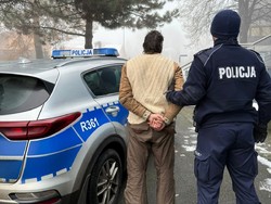 Zdjęcie przedstawia: policjanta z zatrzymanym mężczyzną przy radiowozie.