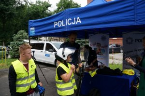 Dzieci w kamizelkach odblaskowych na tle stoiska raciborskiej policji