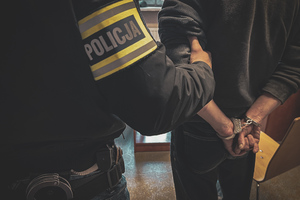 zdjęcie poglądowe - policjant kryminalny trzyma zatrzymanego z kajdankami na rękach
