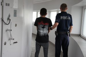 policjant trzyma za rękę podejrzanego. stoją w korytarzu policyjnego aresztu.