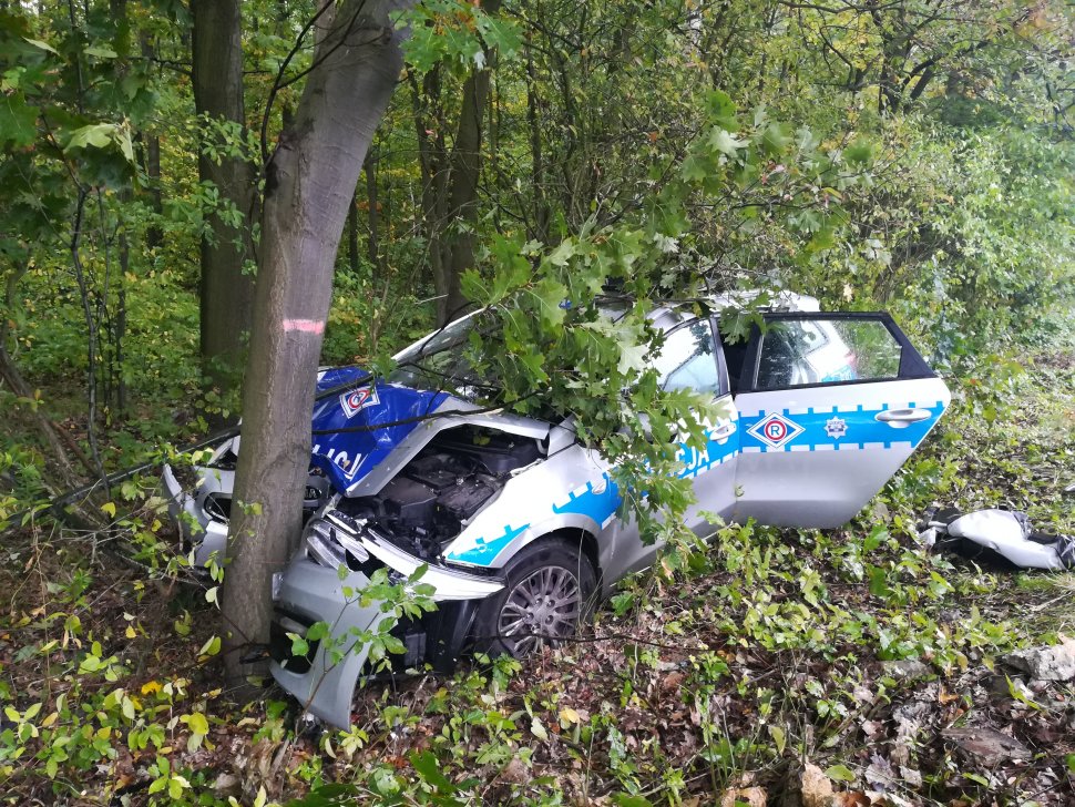 na zdjęciu widać kompletnie zniszczony radiowóz policyjny wbity w przydrożne drzewo. 