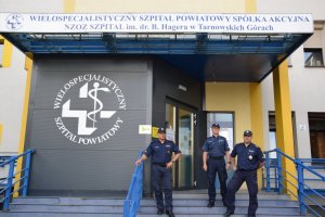 Na zdjęciu widać trzech policjantów stojących przed Wielospecjalistycznym Szpitalem Powiatowym