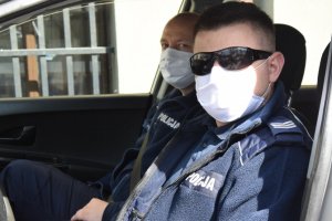 fotografia kolorowa: dwóch policjantów w radiowozie, którzy twarze mają zakryte maseczkami