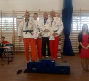 Obrazek przedstawia policjanta stojącego na podium oraz innych zawodników w kimonie na zawodach sportów walki w Wołominie