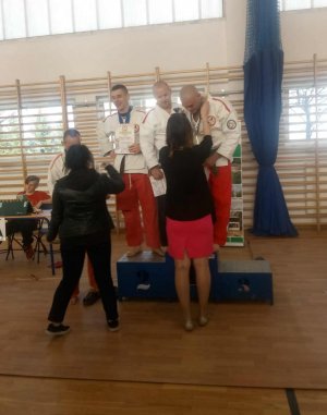 Obrazek przedstawia policjanta stojącego na podium oraz innych zawodników w kimonie na zawodach sportów walki w Wołominie