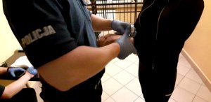Umundurowany policjant zakłada kajdanki zatrzymanej kobiecie.