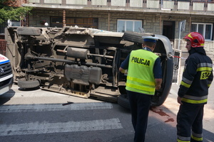 Policjant ruchu drogowego w pobliżu przewróconego na bok volkswagena wykonujący oględziny miejsca wypadku.