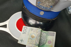 Na zdjęciu widoczna czapka policjanta ruchu drogowego, tarcza do zatrzymywania pojazdów oraz banknot stuzłotowy.