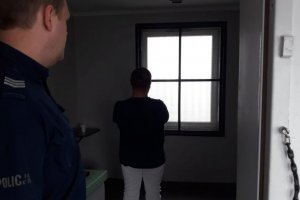 Zatrzymany stoi tyłem w celi, przy drzwiach policjant