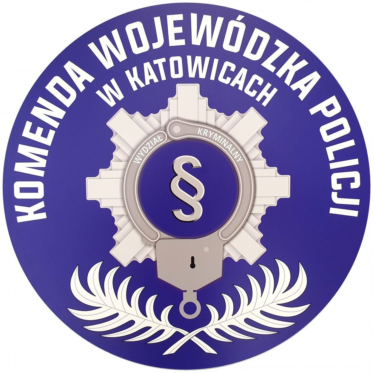 Logo Wydziału Kryminalnego Komendy Wojewódzkiej Policji w Katowicach. Na okrągłym, granatowym tle widoczne kajdanki wokół którego są ramiona policyjnej gwiazdy, w środku paragraf.