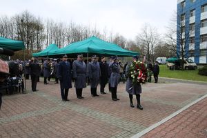 Fotografia kolorowa. Na zdjęciu policjanci oraz zebrani goście składający kwiaty przed grobem.