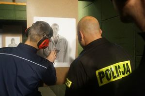 Zdjęcie kolorowe. Sędzia konkurencji strzeleckiej wskazuje przestrzeliny na tarczy funkcjonariuszowi Wydziału Kryminalnego