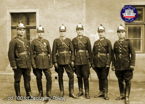 Zdjęcie archiwalne z okresu międzywojennego: policjanci w strojach galowych przed budynkiem