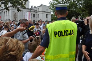 policjant śląskiej drogówki udziela dzieciom rad na temat bezpiecznego przechodzenia przez jezdnię, w tle dziennikarze