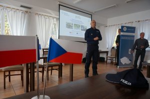 na pierwszym planie flaga Polski oraz Czech i leżąca na stoliku policyjna czapka, w tle jeden z policjantów podsumowujący projekt