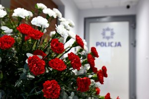 Biało-czerwone kwiaty, w tle drzwi wejściowe do posterunku z logo policji