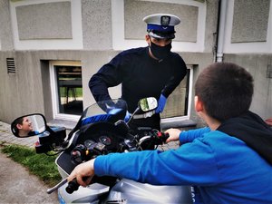 Policjant z drogówki przygląda się chłopcu, który siedzi na motocyklu.