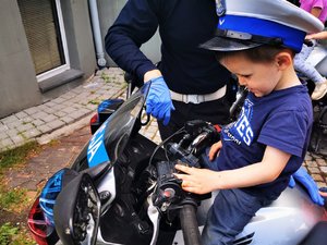 Chłopiec z policyjną czapką siedzi na motocyklu.
