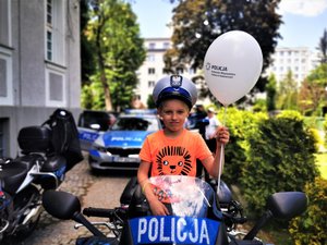 Chłopiec z balonikiem siedzi na policyjnym motocyklu.