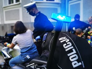 Policjant przygląda się dziecku siedzącemu na policyjnym motocyklu.